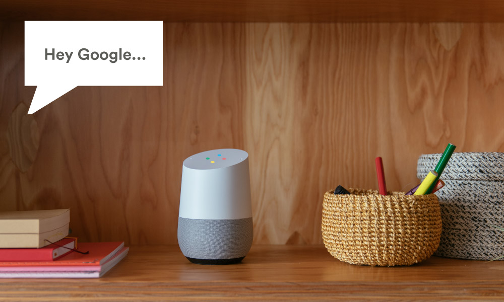 image showing google home voice controller placed on a study table surrounded by a en holder and some books